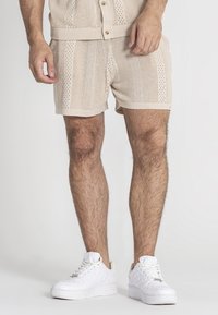 Beige gebreide shorts met openwerk patroon, contrasterende strepen en elastische tailleband. Gecombineerd met witte sneakers.