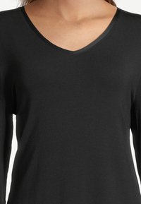 Woman wearing a fitted long-sleeve black V-neck shirt, shown from the shoulders to mid-torso against a plain background.