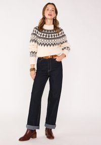 Maglione lavorato a maglia in crema con motivi geometrici grigi, abbinato a jeans di denim scuri con risvolti. Stivaletti in pelle marrone completano il look.