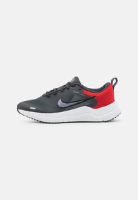 Baskets de sport noires et grises avec une tige en maille respirante, des accents rouges au talon, des lacets noirs et une semelle intermédiaire blanche, conçues pour le confort et le soutien.
