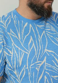 Hellblaues Baumwoll-T-Shirt mit einem cremefarbenen Blattmuster, geripptem Rundhalsausschnitt und kurzen Ärmeln mit einer weichen Textur.