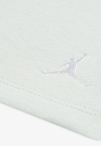 Svijetlozelena tekstilna površina s teksturiranim finišem, s bijelim izvezenim Jumpman logotipom u dinamičnoj pozi u donjem kutu.