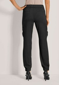 Schwarze Cargo-Hosen mit einem lockeren Schnitt, ausgestattet mit einem elastischen Bund, seitlichen Taschen und elastischen Bündchen an den Knöcheln. Glatte Stofftextur.