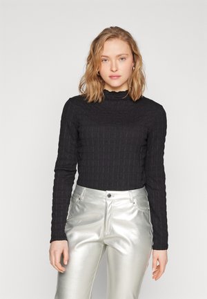 Black textured long-sleeve top with a high collar, paired with shiny silver pants featuring a classic five-pocket design.