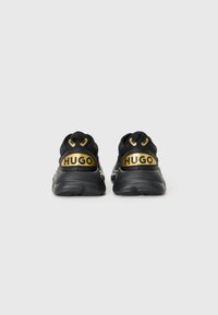 Black sneakers with gold accents and branding. Features a textured rubber sole and a smooth fabric upper with a padded collar.