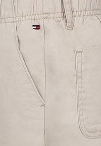 Pantaloni beige con elastico in vita, tasche laterali e una piccola etichetta con logo. Presentano un tessuto morbido e semplici dettagli di cucitura.