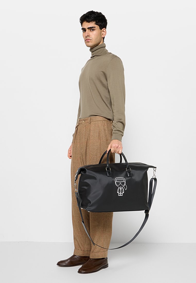 Bolsa impermeable negra con doble asa y correa ajustable para el hombro. Presenta una figura de dibujos animados blanca impresa en el frente. Textura lisa.