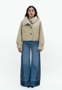 Beige cropped jack met een grote shearling kraag, met drie knopen en brede blauwe denim flared broeken met paneel details.