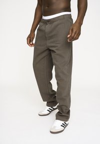 Brune, afslappede bukser med knap og elastisk talje, der har sidelommer og lige ben. Båret med hvide og grå sneakers.