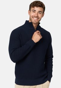 Suéter de punto azul marino con cuello alto y media cremallera. Presenta puños y dobladillo acanalados, fabricado con un tejido texturizado.