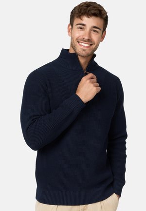 Suéter de punto azul marino con cuello alto y media cremallera. Presenta puños y dobladillo acanalados, fabricado con un tejido texturizado.