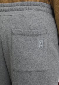 Grijze joggingbroek met een achterzak en een lichtblauw geborduurd logo, gemaakt van een zachte, gestructureerde stof. Elastische tailleband zichtbaar.