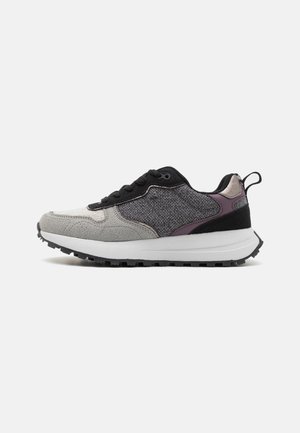 Sneaker featuring a mix of grey suede and textured black material, with a purple accent, black laces, and a rugged black sole.
