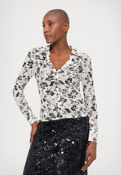 Long-sleeve blouse featuring a black and white floral pattern, button-down front, and textured fabric. Worn with a sequined dark navy skirt.