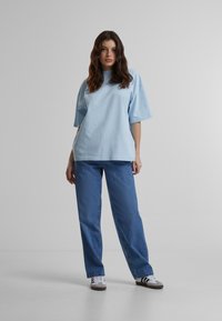 Camiseta de algodón de color azul claro, de corte oversize y con mangas cortas, combinada con unos vaqueros rectos azules. Las zapatillas blancas tienen rayas negras.