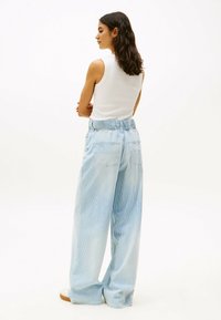 Pantalones de pierna ancha a rayas en azul claro con cintura elástica y bolsillos traseros, combinados con una blusa ajustada sin mangas blanca.