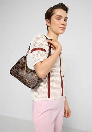 Sac à main à motif géométrique marron avec une bandoulière en chaîne dorée, texture lisse et silhouette douce, tenu par une personne portant un haut en tricot blanc.