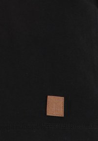 Zwarte katoenen t-shirt met een bruine vierkante leren patch met geperst merklogo, schone randen en een zachte textuur.
