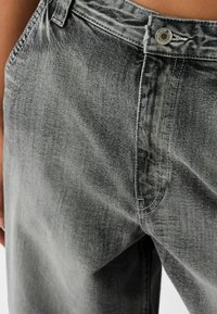 Szare dżinsy z denimu o luźnym kroju, z wyblakłą fakturą, zapinane na górny guzik, z widocznymi przeszyciami wzdłuż szwów.