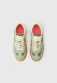 Grønne nubuck sneakers med nettdetaljer, kremfargede lisser og såle av gummigummi. Innvendig har de en rosa såle. Bølgemønster på sidene.