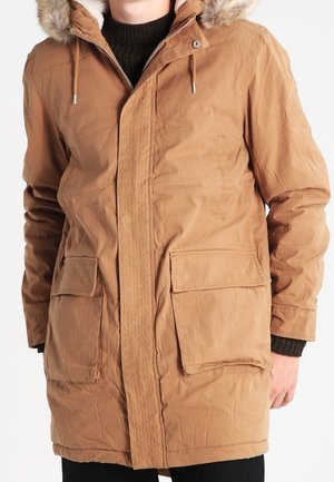 Parka acolchada de color marrón, con capucha forrada de pelo sintético, cremallera frontal y dos bolsillos tipo parche; presenta una tela texturizada y un corte relajado.