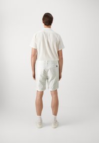Kortsleeve hvit teksturert skjorte og lyse shorts, med baklomme og rullede sømmer, kombinert med hvite sneakers.