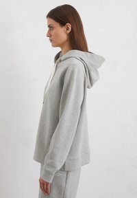 Grijze hoodie met een zachte textuur, zijaanzicht, met een kangoeroe-pocket en contrasterende witte trekkoorden.
