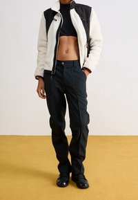 Kurtka polarowa w odcieniu off-white i czerni, krótki krój z zapięciem na zamek. Czarna spódnica z kieszeniami z przodu, prosty krój, noszona z czarnymi butami.