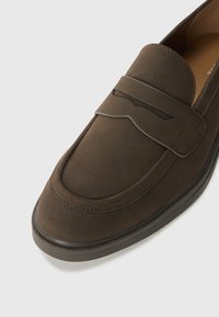 Brown suede loafers with a smooth finish, featuring a decorative band across the upper and contrast stitching along the edges.