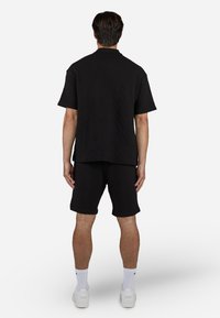 Black short-sleeve polo shirt and matching shorts, both with a diamond-patterned texture. Accessories include white socks and sneakers.