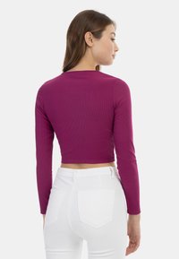 Tætsiddende, langærmet, cropped top i ribbet blommefarvet stof. Kombineret med hvide højtaljede jeans med baglommer.
