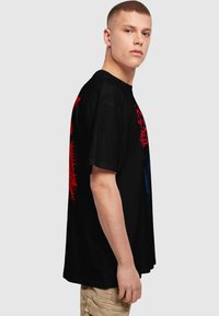 Sort bomulds t-shirt med lyse røde og blå grafiske designs på ryggen. Korte ærmer og en afslappet pasform.