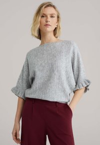 Pull surdimensionné gris clair avec manches côtelées, porté avec un pantalon bordeaux. Texture douce avec une coupe décontractée et un large décolleté.
