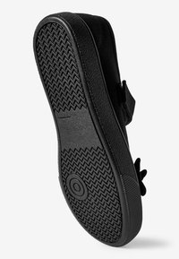 Semelle de chaussure noire avec un motif de grip texturé, présentant un bord arrondi et un design plat. Une bande Velcro est visible en haut pour un maintien sécurisé.