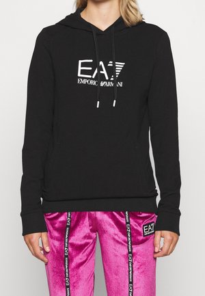 Czarna bluza z kapturem EA7 Emporio Armani ze sznurkami w zestawieniu z błyszczącymi różowymi spodniami z czarnymi, pionowymi paskami z logo EA7.