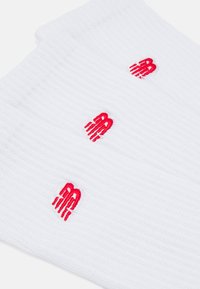 White ribbed socks featuring red embroidered logo. Textured fabric with three logos distributed evenly across the surface.