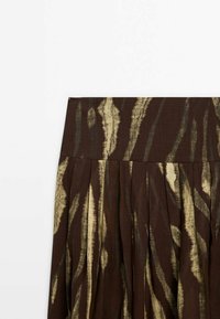 Bruine geplooide rok van een gestructureerde stof, met een gouden abstract patroon, een brede tailleband en een vloeiende uitstraling.