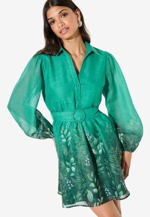 Groen linnen overhemdjurk met doorschijnende lange mouwen, een taille met ceintuur en een zoom met bloemenprint. Heeft een knoopsluiting aan de voorkant en een losse pasvorm.