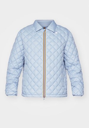 Világoskék steppelt dzseki cipzárral, alatta sötétkék kapucnis pulóver, és tengerészkék cargo nadrág. A szettet fehér sportcipők egészítik ki.