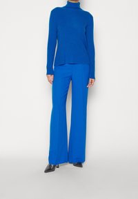 Pull à col roulé côtelé bleu associé à un pantalon large bleu. La tenue présente une couleur harmonieuse et une coupe contemporaine.