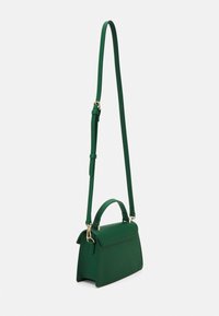 Liten strukturerad grön crossbody-väska med handtag upptill, justerbar lång rem och guldfärgade detaljer på vit bakgrund.