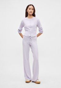 Λιλά πλεκτή ζακέτα με κουμπιά, συνδυασμένη με ταιριαστά ψηλόμεσα παντελόνια φαρδιάς γραμμής. Ομαλή υφή, άνετη εφαρμογή, μίνιμαλ σχεδιασμός.