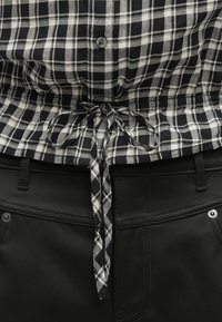 Πουκάμισο με κουμπιά σε ασπρόμαυρο καρό μοτίβο με σφικτή μέση και ζώνη. Συνδυάζεται με μαύρο παντελόνι που αναδεικνύει τις τσέπες και τις λεπτομέρειες με ραφές.