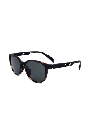Occhiali da sole rotondi con lenti scure, montatura frontale tartarugata e aste nere con piccolo logo Adidas dorato sul lato.