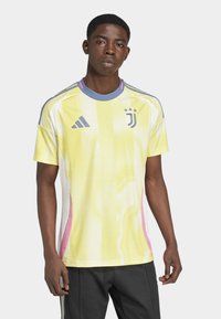 Gul nätjacka med blå och rosa detaljer, tre stjärnor och logotyp på bröstet, korta ärmar och rund halsdesign.