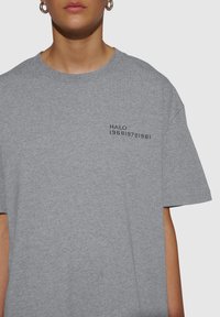 Grijze katoenen t-shirt met een ontspannen pasvorm. Kenmerkt een bedrukte zwarte logo "HALO 196819721981" aan de linkerkant van de borst. Korte mouwen.