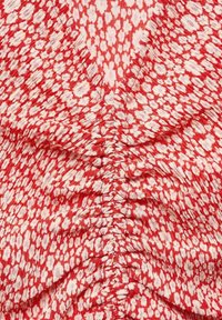 Tela roja con un diseño floral, que presenta una textura recogida y un ligero brillo, creando una apariencia drapeada y fluida.