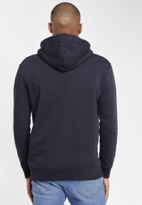Mörkblå hoodies med ribbade ärmslut och linning, slät tygtextur, och en känguruficka som inte syns i denna vy.