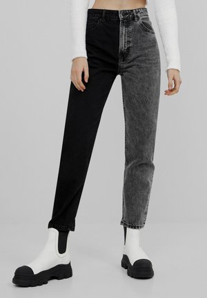 Frau trägt hochgeschnittene Jeans mit einem schwarzen Bein und einem grauen, säuregewaschenen Bein, kombiniert mit weißen Stiefeln mit schwarzen Sohlen.