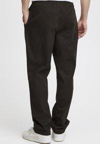 Sorte bomullsbukser med elastisk midje, rett ben-design og en enkel baklomme. Brukt med hvite joggesko.